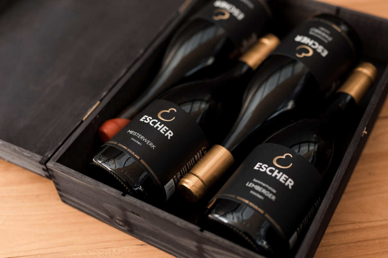 Foto von vier Flaschen GOLDLAGE Wein in einer schwarzen Holzkiste auf einem Holztisch des Weingut Escher Schwaikheim bei Stuttgart im Rems-Murr-Kreis zur Veranschaulichung von Probierpaketen, Foto ist von Sarah Escher Fotografie https://sarah-escher-fotografie.de/